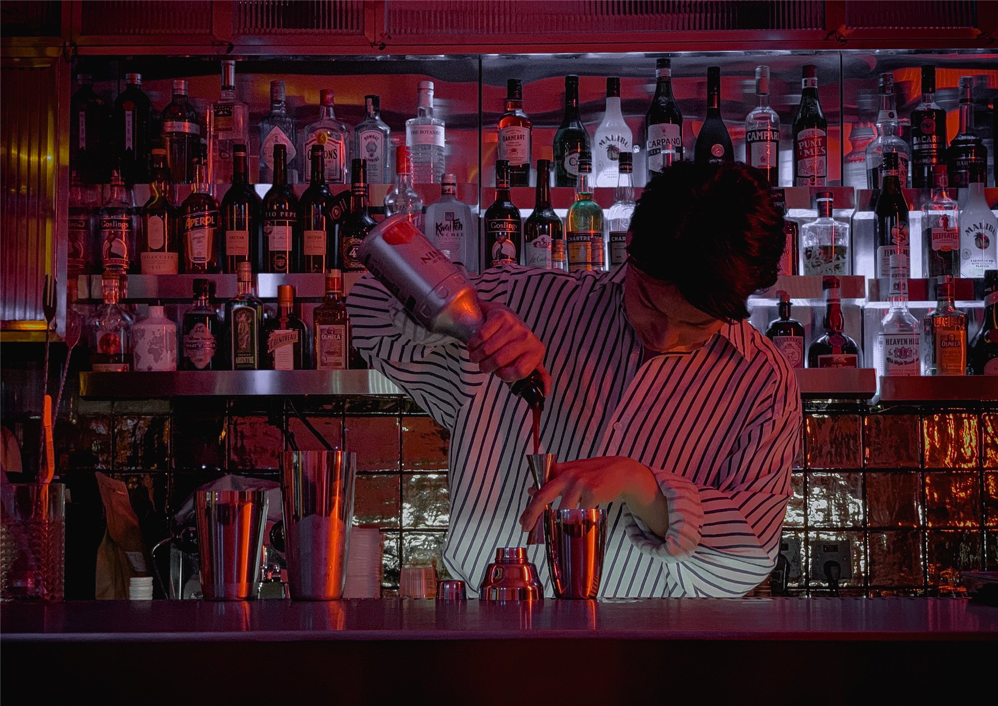 Bartender shaking a cocktail at the red-lit back bar