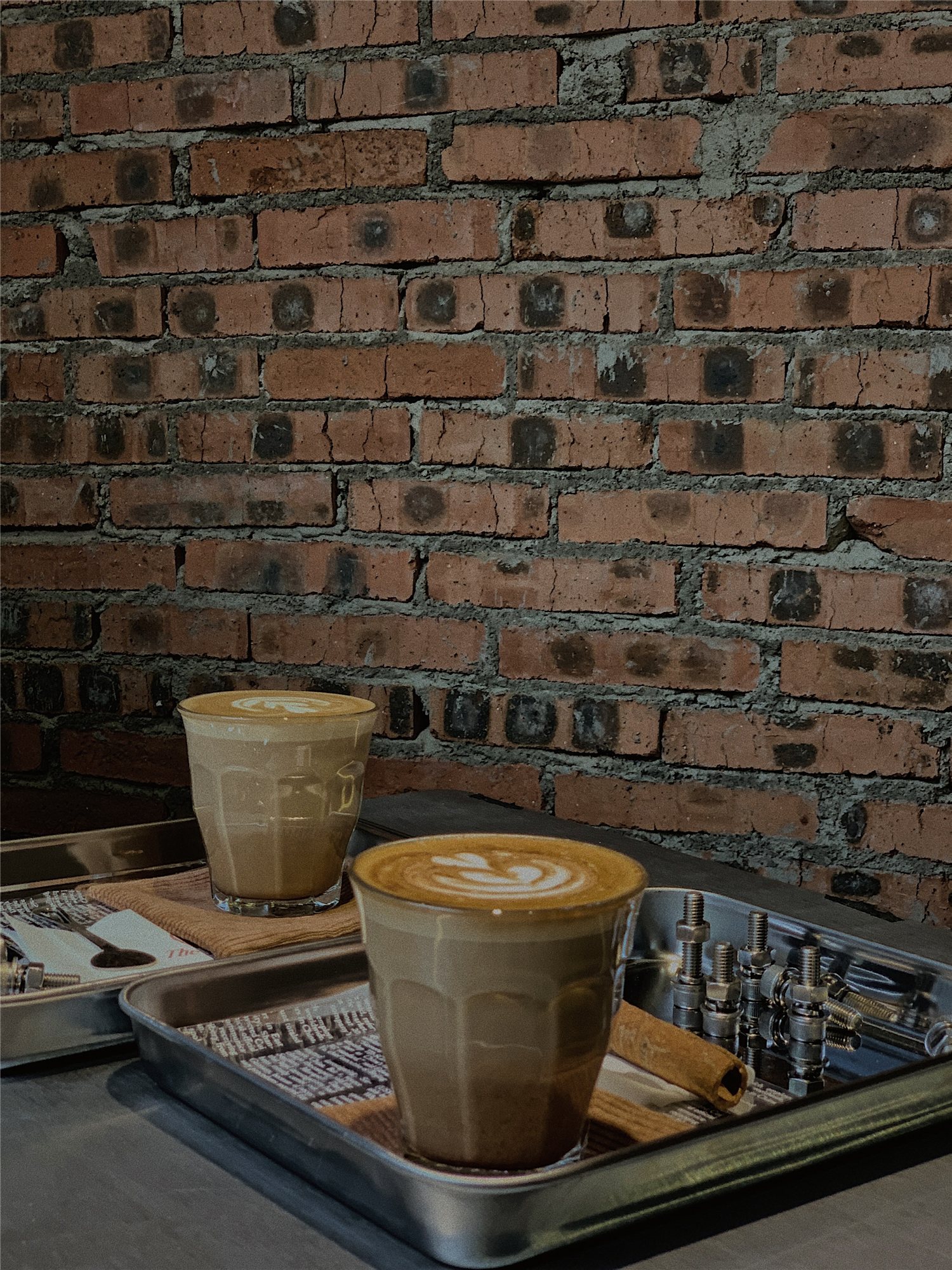 Two lattes on a steel tray against the raw brick wall